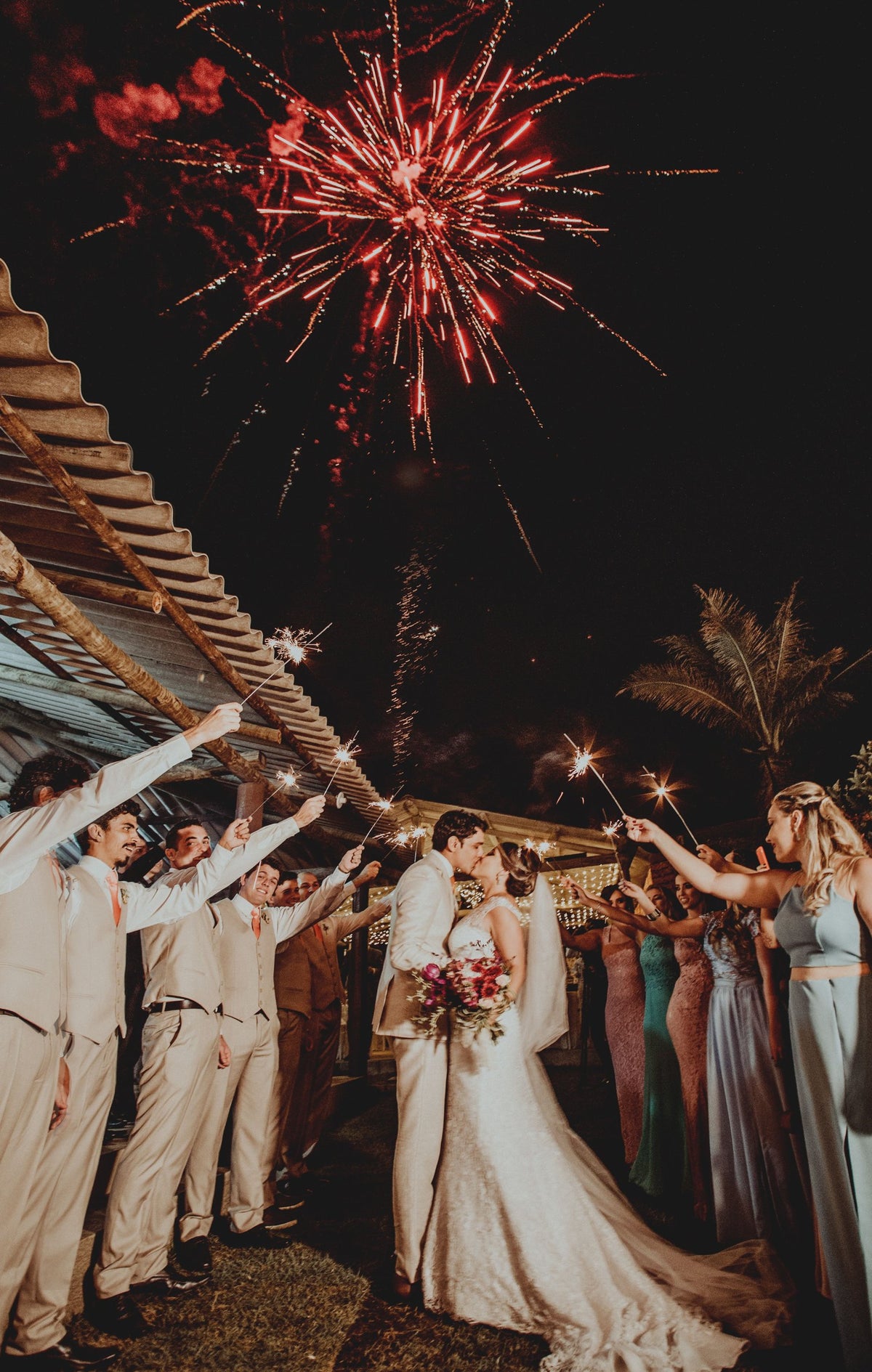 Bride and groom kiss as guests hold lit sparklers at a wedding send-off